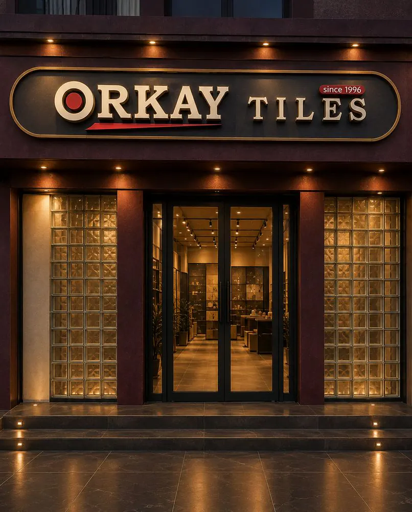 Lit ORKAY Tiles showroom facade at night, gold-lettered sign above glass-block windows